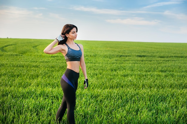 Een meisje met mooie lichaamsvormen op een achtergrond van groen gras in een sportuniform buiten de stad in de natuur een actieve levensstijl