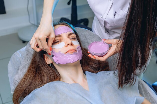 Een meisje met verkoelende plekken onder haar ogen krijgt een spaservice van een schoonheidsspecialiste die een masker maakt voor het hele gezicht.