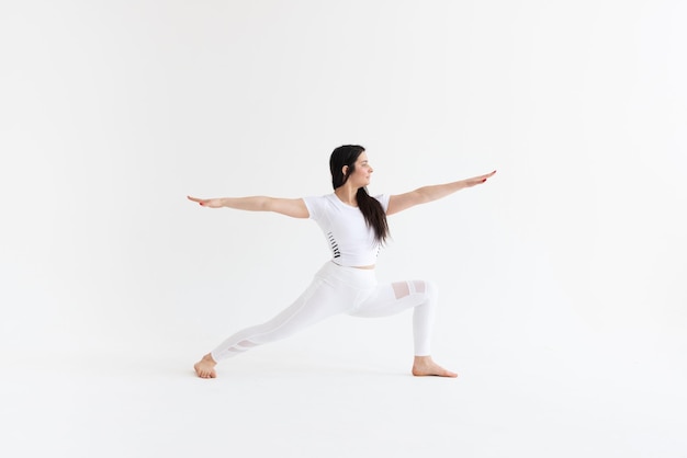 Een meisje op een witte achtergrond in de pose van warrior pose ii virabhadrasana ii