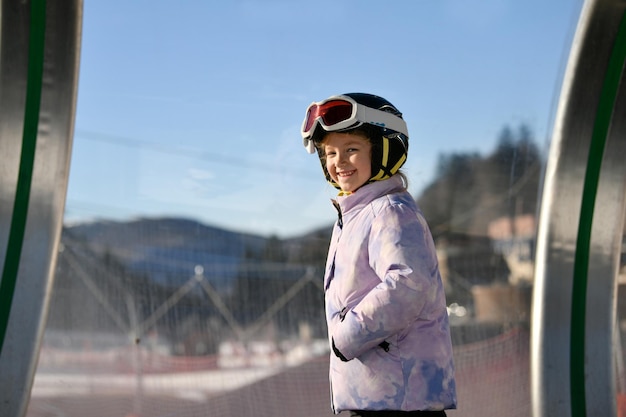 Een meisje op ski's staat op een tapijt-skilift in een glazen tunnel