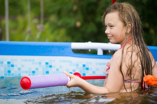 Een meisje schiet op een zomerdag met een waterpistool in het zwembad