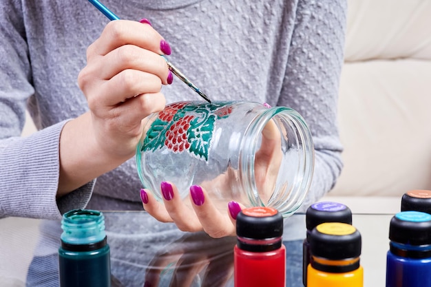 Een meisje schildert een glazen pot met glas-in-loodverf