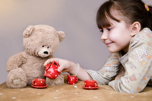 Een meisje speelt met een beer, het meisje lacht en schenkt thee in bij een speelgoedbeer