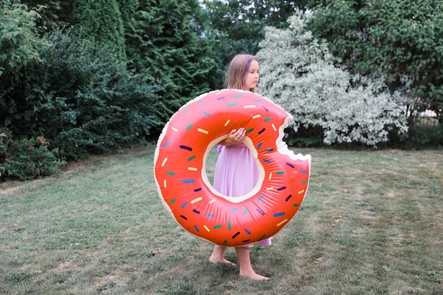 Een meisje speelt met een opblaasbare cirkel met een dout in de tuin op een warme zomerdag.