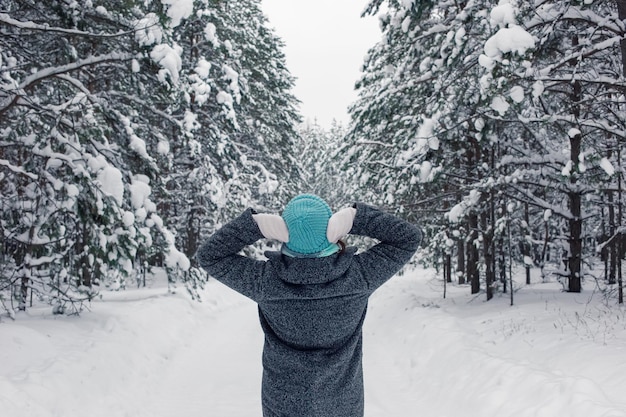 Een meisje staat in een prachtig besneeuwd winterbos en steekt haar handen naar haar hoofd en onderzoekt de bomen
