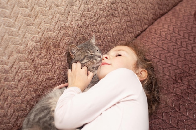 Een meisje van 6 jaar ligt op de bank en knuffelt een kat