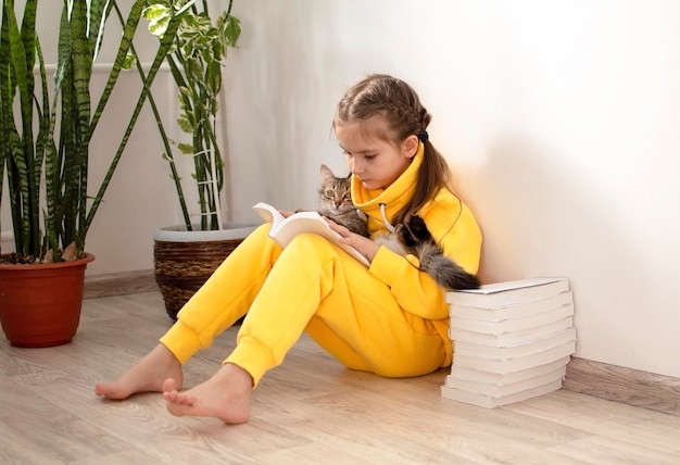 Een meisje van de lagere school houdt een kat in haar armen en zit naast een stapel boeken. Het kind leert lezen en schrijven. Het concept van onderwijs, studie, huiswerk, levensstijl.