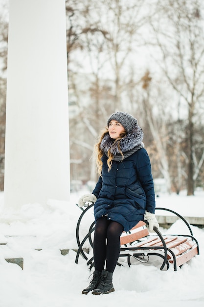 Een meisje van Europese uitstraling loopt in het park, bos, winter en sneeuw, gekleed in warme kleding, hoed, jas, sjaal, rust, wandelen