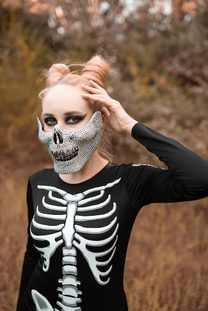 Een meisje verkleed als een skelet met een masker met strass-steentjes kijkt eng in de camera Halloween