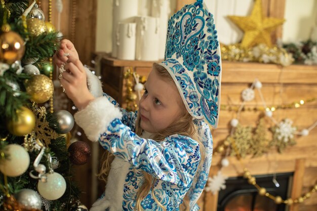 Een meisje versiert een kerstboom in een sneeuwmeisjeskostuum voor de nieuwjaarsvakantie in blauwe tinten