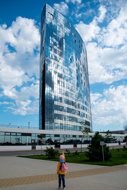 Een meisje voor een groot modern gebouw tegen een blauwe hemel. Moderne architectuur. Stad.