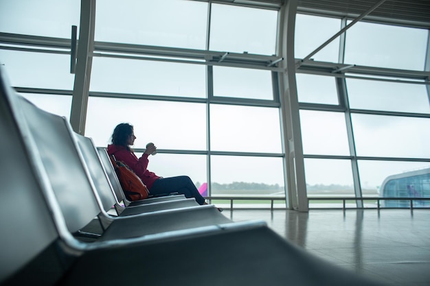 Een meisje zit op een lege rij stoelen voor een groot glas-in-loodraam in een luchthaventerminal, wachtend op een vlucht