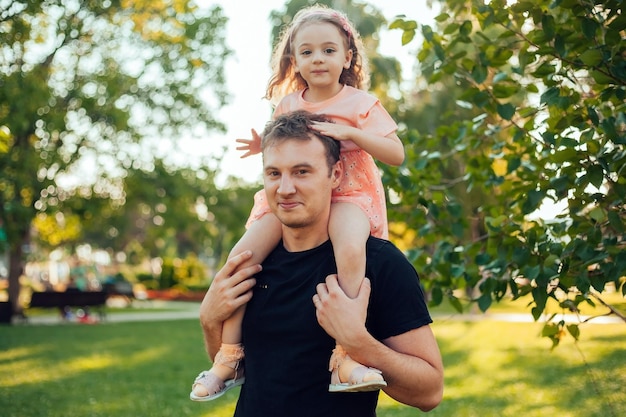 een meisje zit op vaders schouders tijdens een wandeling in een zomerpark