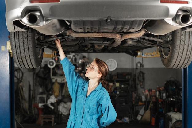 Een meisjesautomonteur met een bril in de garage controleert de bevestiging van de wielen en de integriteit van het chassis in een autowerkplaats Autoreparatie in de garage Vrouw in werkkleding