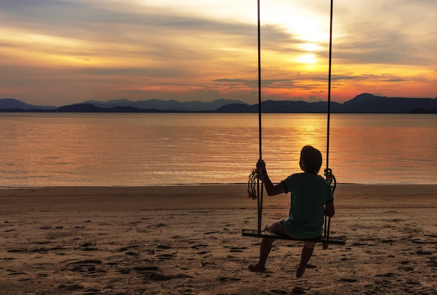 Foto een mens die op houten schommelingsstoel ontspant die zonsondergang op strand kijkt