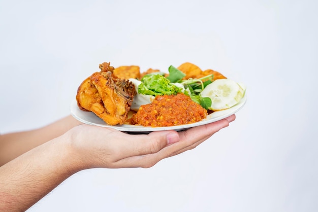 Een menselijke hand die een bord vasthoudt met pecel ayam gebakken tempe en tofu met een witte achtergrond Traditioneel Indonesisch eten