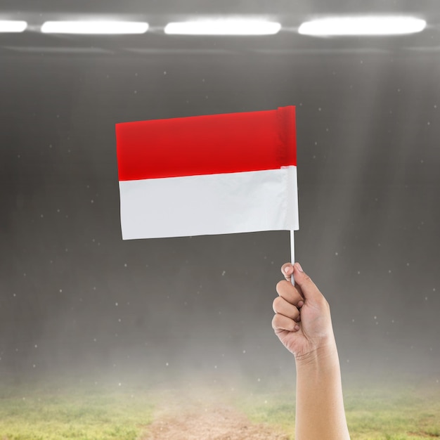 Een menselijke hand die een Indonesische vlag vasthoudt met een schijnwerper als achtergrond Indonesische onafhankelijkheidsdag