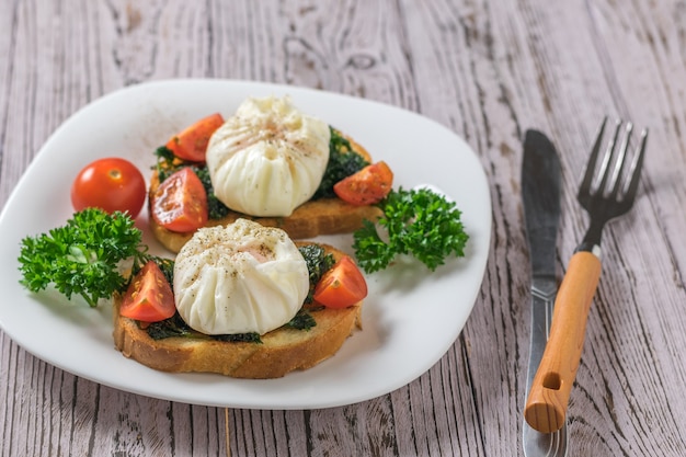 Een mes en vork en twee sneetjes gebakken brood met gepocheerde eieren op een houten tafel. vegetarische snack met gepocheerde eieren.