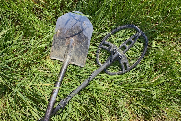 Foto een metaaldetector en een schop voor het zoeken naar munten en edele metalen producten liggen gekruist op het groene gras