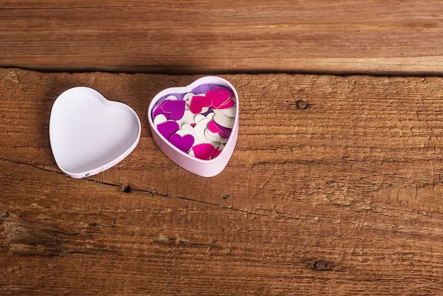 Een metalen doos in de vorm van een hart met valentijnskaarten. Helder effen gekleurd papier op een houten oppervlak