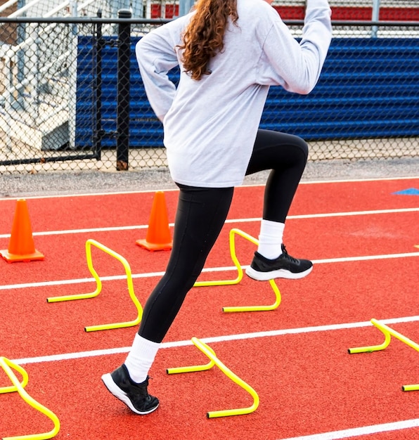 Een middelbare school meisje stapt over gele mini hindernissen tijdens snelheid en behendigheid oefening
