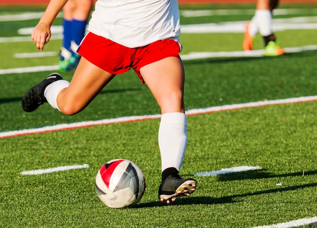 Foto een middelbare school tienermeisje op het punt om een voetbal te schoppen tijdens een wedstrijd op een groen grasveld