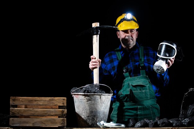 Foto een mijnwerker houdt een pik in de ene hand en een stofmasker in de andere op een zwarte achtergrond