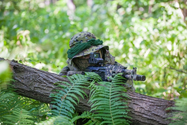 Een militair in het bos zit in een hinderlaag. Soldaat machinegeweer en kleren