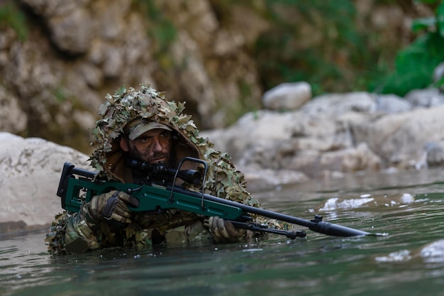 Een militair of airsoftspeler in een camouflagepak sluipt over de rivier en richt met een sluipschuttersgeweer opzij of op doel.