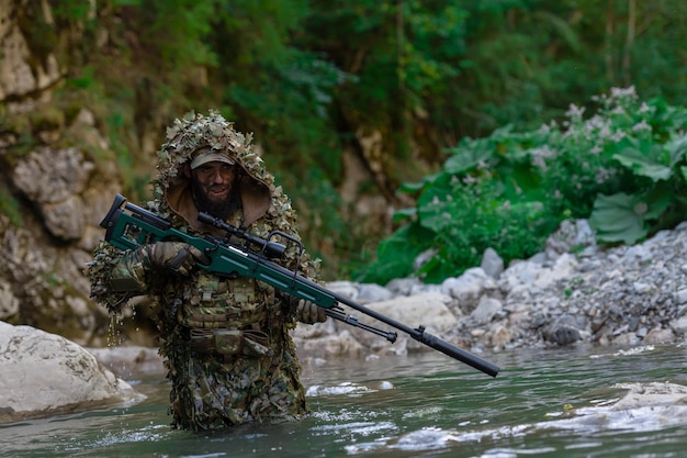 Een militair of airsoftspeler in een camouflagepak sluipt over de rivier en richt met een sluipschuttersgeweer opzij of op doel.