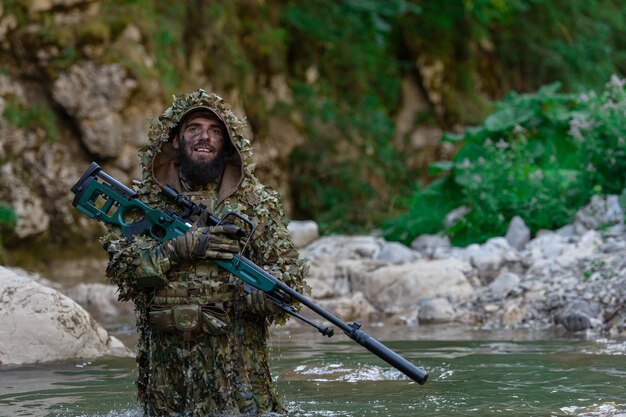 Een militair of airsoftspeler in een camouflagepak sluipt over de rivier en richt met een sluipschuttersgeweer opzij of op doel.