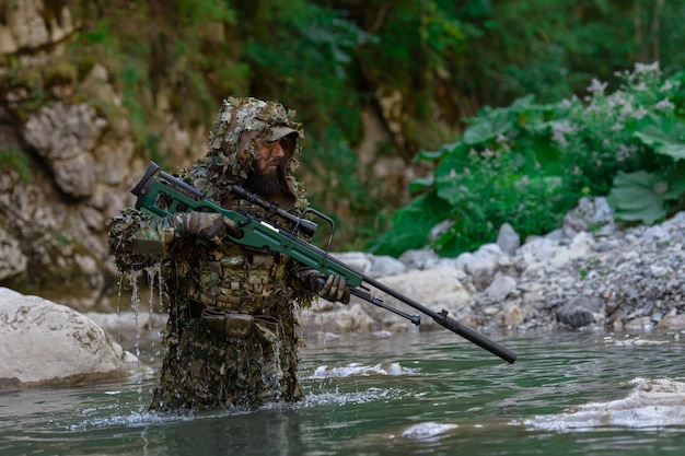 Een militair of airsoftspeler in een camouflagepak sluipt over de rivier en richt met een sluipschuttersgeweer opzij of op doel.