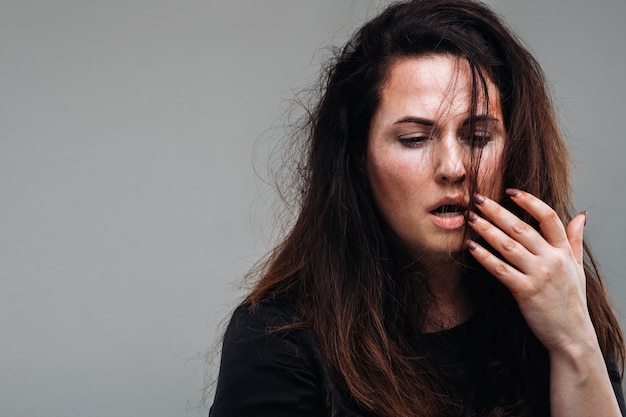 Een mishandelde vrouw in zwarte kleren op een geïsoleerde grijze muur. Geweld tegen vrouwen.