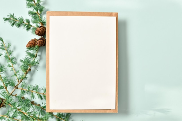 Een mockup van een kraft-envelop met een blanco vel en een tak van groene lariks op een lichtblauwe achtergrond