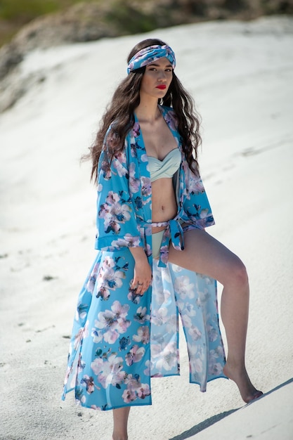 Een model draagt een blauwe bloemenkimono op het strand.