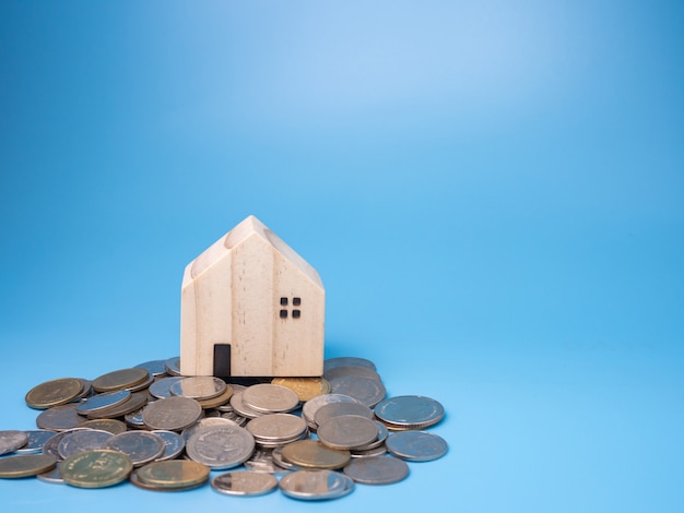 Een model houten huis en een stapel munten op blauw