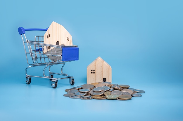 Een model houten huis op een winkelwagentje Met een stapel munten op blauw