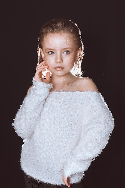 Een modelmeisje in een witte blouse met pailletten op haar huid poseert op een zwarte achtergrond