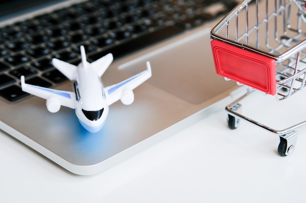 Een modelvliegtuig staat op een laptop naast een trolley. Het kopen van kaartjes voor een vlucht via internet.