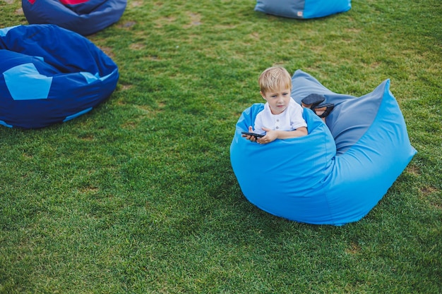 Een modern kind met een gadget Een jongetje zit op een zonnige dag buiten spelletjes te spelen aan de telefoon