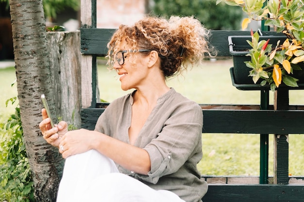 Een moderne dame met behulp van mobiele telefoon buiten huis in de tuin genieten van draadloze verbinding en communicatie Video-oproep mensen in outdoor technologie vrijetijdsbesteding alleen Een vrouw met mobiele telefoon