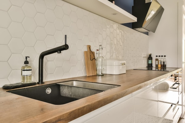 Een moderne keuken met witte hexagon tegels op de muur en houten aanrecht zwarte kraan kraan