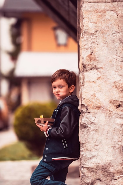 Een moderne kleine jongen poseert in de stad terwijl hij verse, smakelijke poffertjes eet Selectieve focus