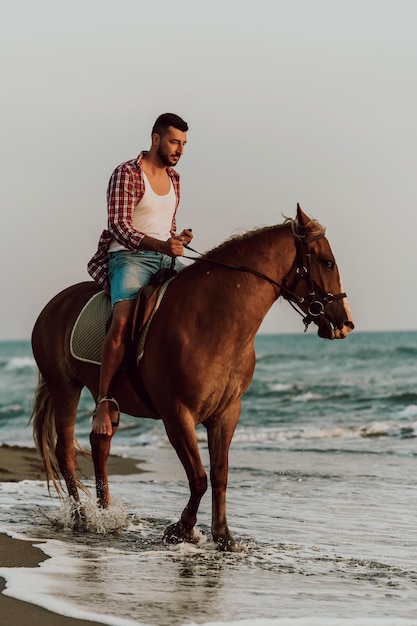 Een moderne man in zomerkleren geniet van het paardrijden op een prachtig zandstrand bij zonsondergang. Selectieve aandacht. Foto van hoge kwaliteit