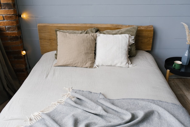 Een moderne Scandinavische grijze slaapkamer met pastelkleurig beddengoed en kussens. Houten bed