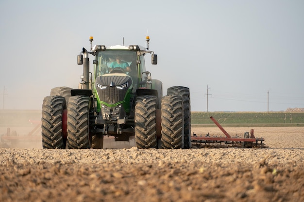 Een moderne tractor met een getrokken ploeg werkt in het veld Het land ploegen voor het zaaien van graangewassen Jonge boer tractorchauffeur van landbouwproductie