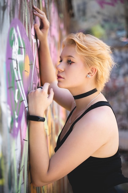 Een modieus meisje met een helder kort kapsel en openhartige make-up poseert tegen de achtergrond van een graffitimuur