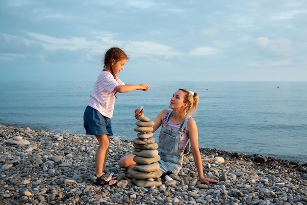 Een moeder en dochter van 6 jaar oud bouwen op het strand een kasteel van stenen Familie zomervakantie