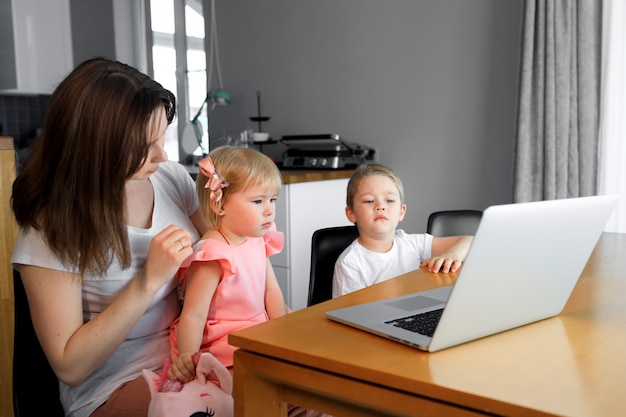 Een moeder met een jonge zoon en dochter kijken naar educatieve programma's op een laptop.