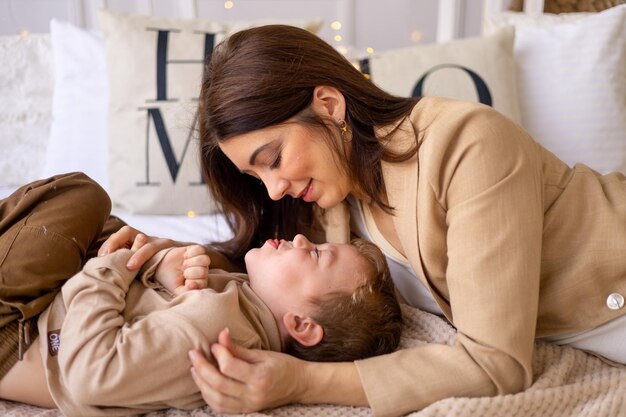 Een moeder met een kleine babyjongen speelt knuffel en kus thuis op een bed in natuurlijke bruine tinten een gelukkig gezin met een klein kind heeft samen plezier